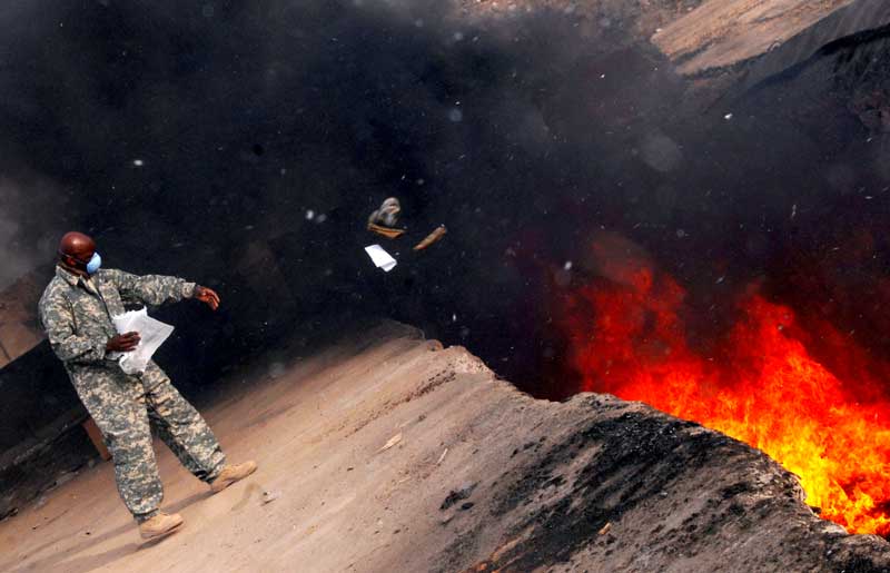 active duty service member wearing mask throwing items into burn pit