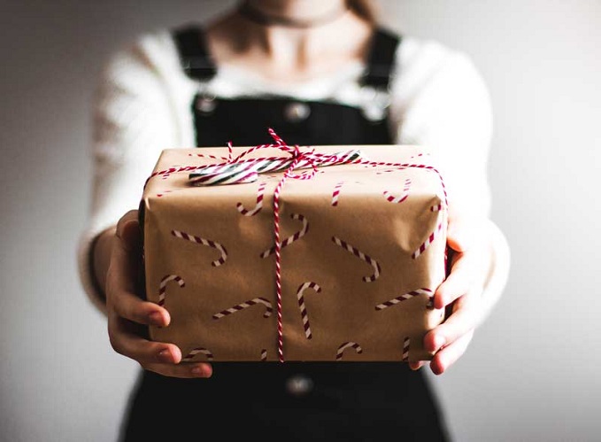 Child offers gift, wrapped in brown paper with candy canes