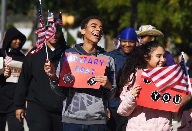 During a Veterans Day parade, a group of young community members show support to our honorable Veterans A small group of onlookers positively cheers on Veterans in a parade setting