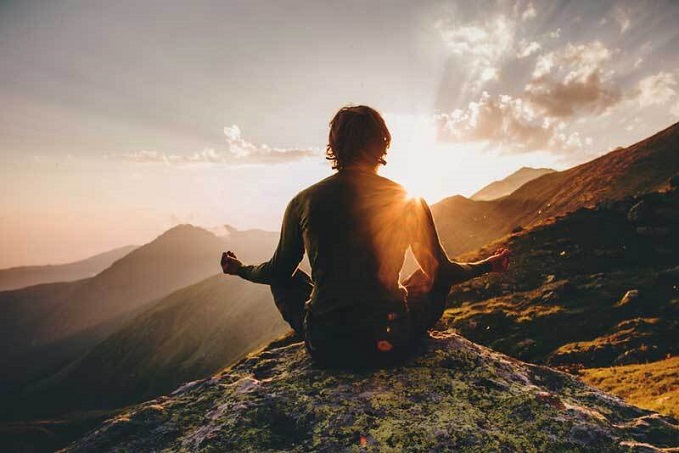 Person meditates on mountain at sunrise