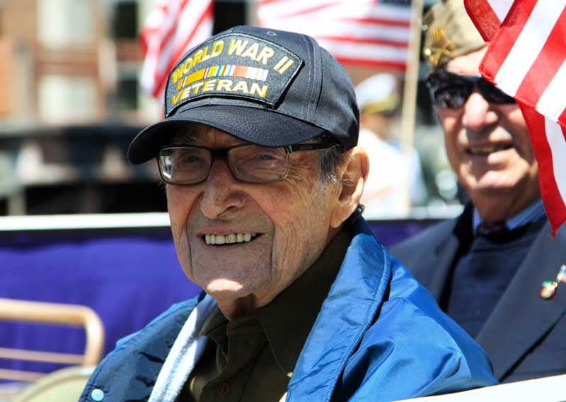 A World War II Veteran smiles at the camera to take a photo during a Veterans Day parade. a world war ii veteran smiles at the camera