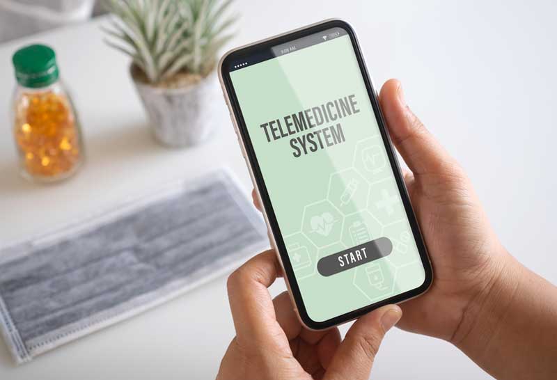 A Veteran uses their cell phone to access a telemedicine system. There is a mask on a table in the background. cell phone used for telemedicine, mask in background