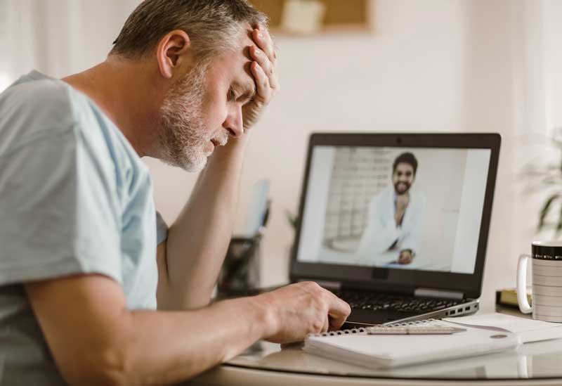 A Veteran sits at his desk watching a video of telehealth providers as he researches his options. veteran researches healthcare