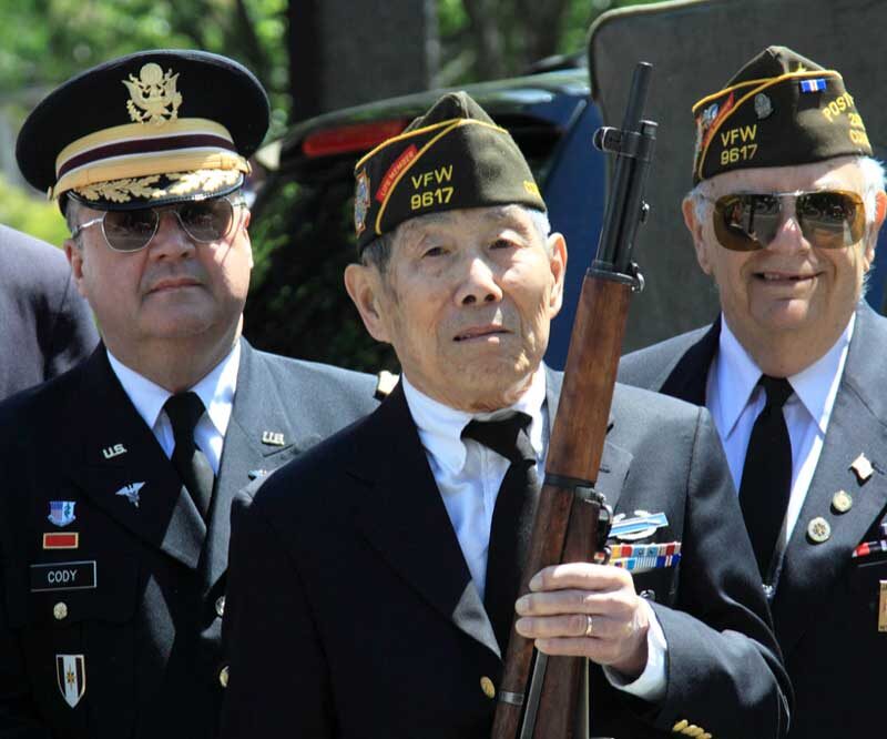 Three Veterans pictured, Veteran in the foreground holding a rifle
