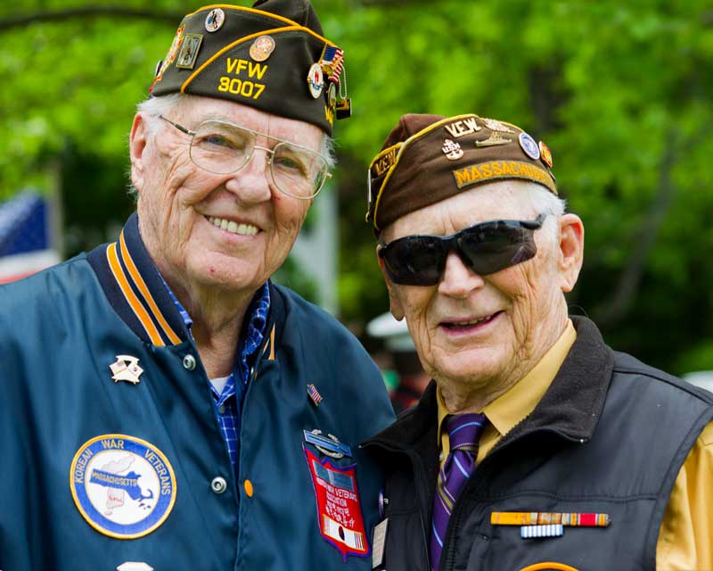 An elderly Korean War Veteran smiles at the camera with a fellow Veteran at a Veterans Day Parada An elderly Korean War Veteran smiles at the camera with a fellow Veteran