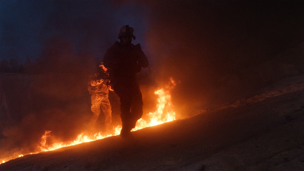 Military members walking around a fire or burnpit.