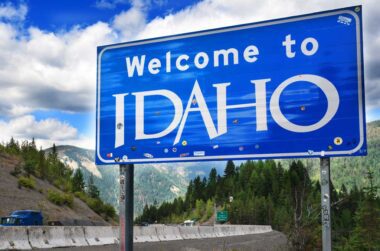 Blue and white "Welcome to Idaho" road sign with green mountains in the background.