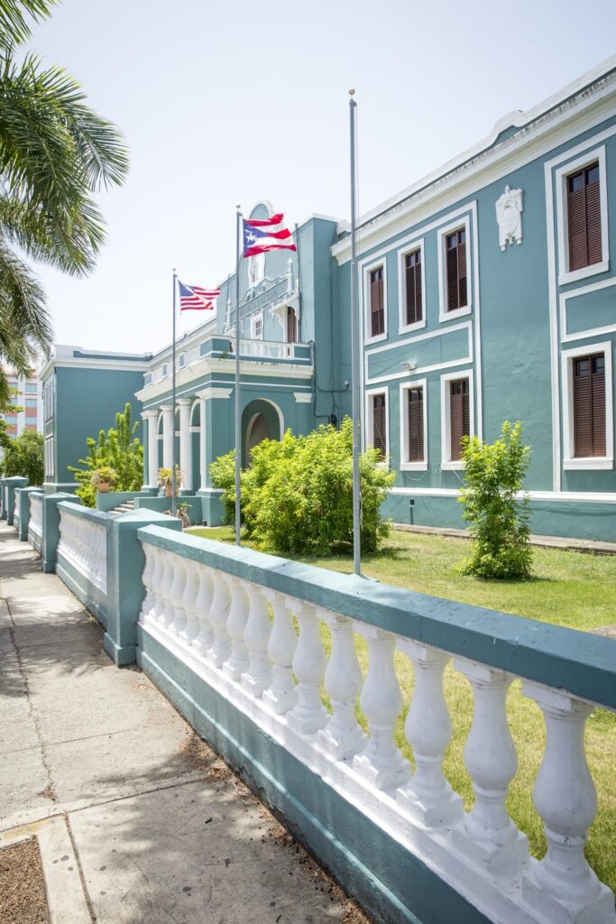 Teal blue Puerto Rico government building with American and Puerto Rico flags flying out front.