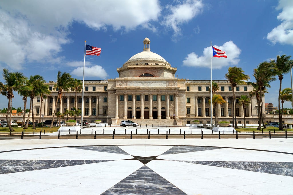 Puerto Rico government building with American and Puerto Rico flags flying in the blue sky out front.