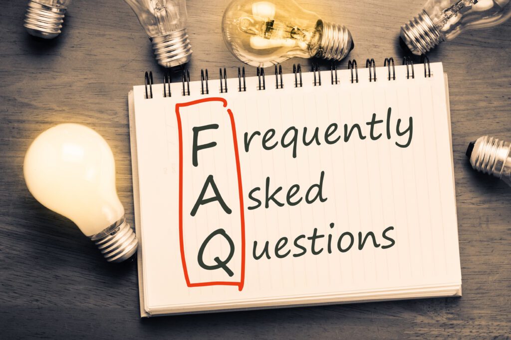 Frequently Asked Questions (FAQ) written on a notebook with lightbulbs on a table.