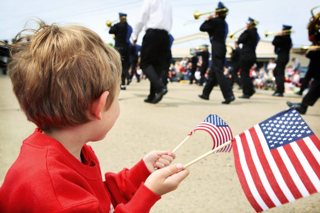 MEMORIAL DAY IMAGE of a boy holding US flags at a parade.