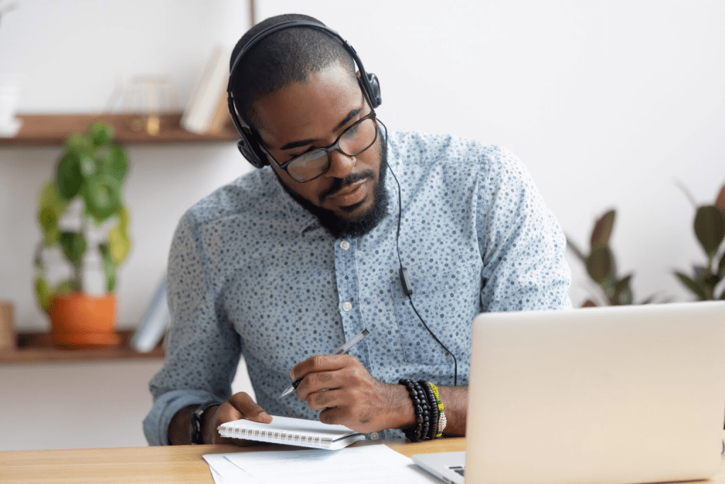 Man with headphones on taking notes on laptop.