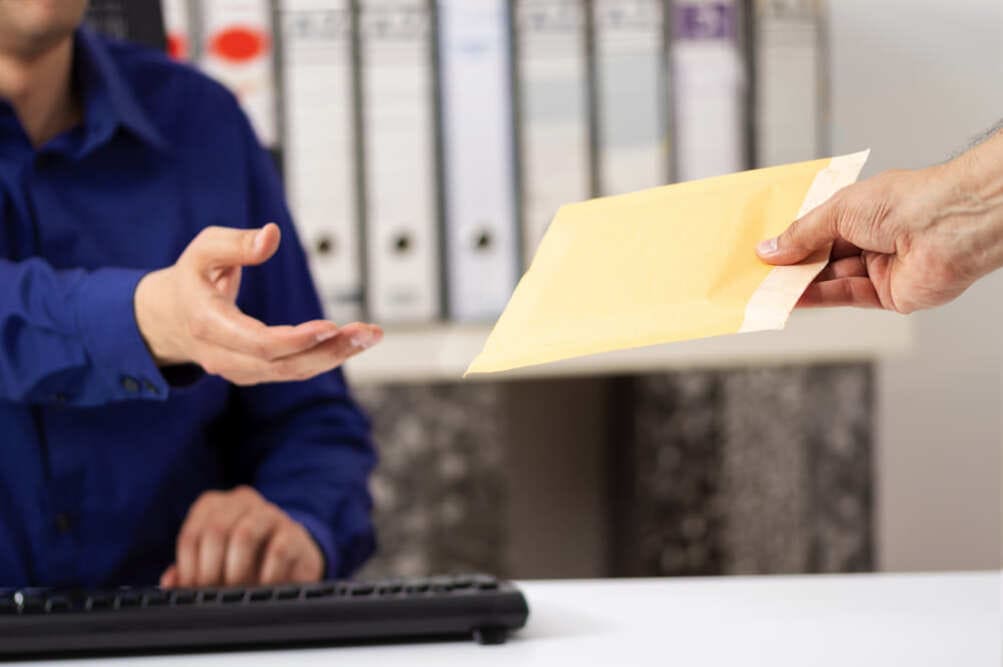 Someone handing a sealed manilla envelope to another person.