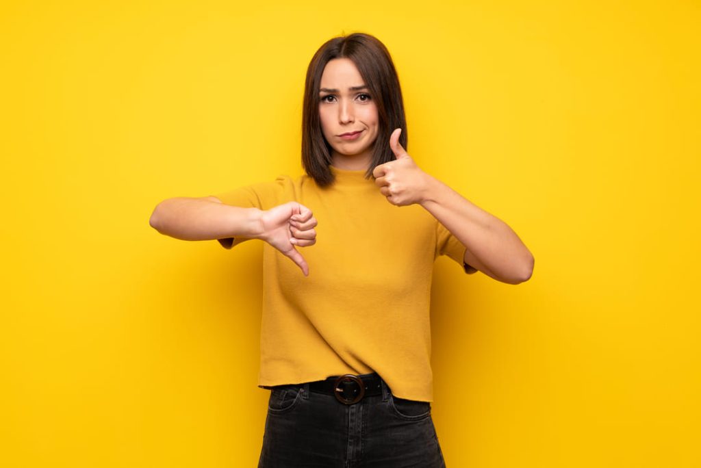 Girl in yellow shirt with yellow background and one thumbs up and one thumbs down.