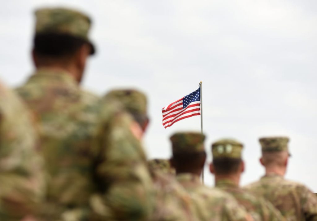 US military members facing american flag.