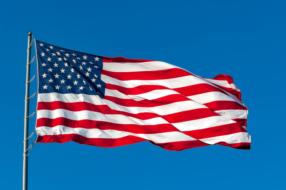 An,American,Flag,Flying,In,The,Breeze,Against,A,Cloudless sky.