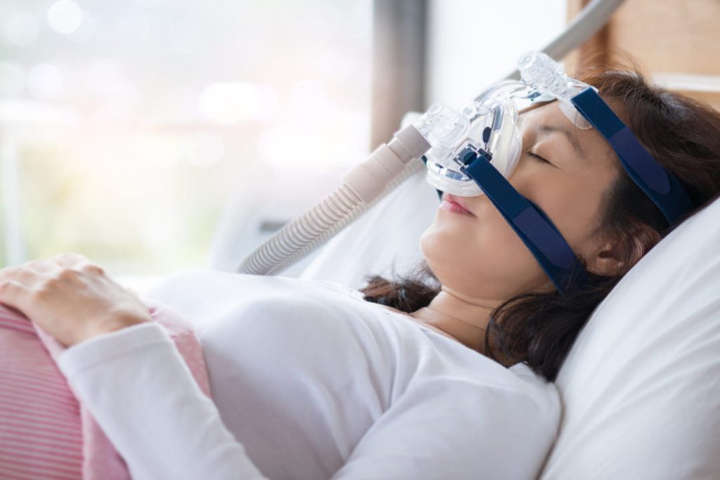 Women with sleep apnea in bed wearing cpap machine.