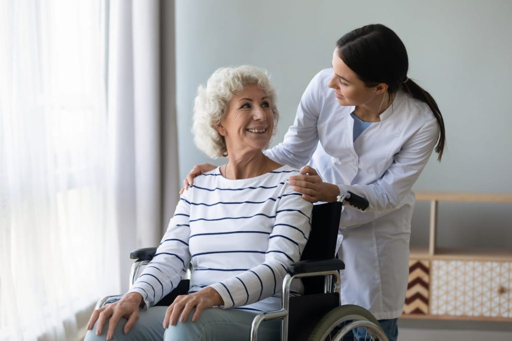 Older lady in wheelchair smiling at nurse.